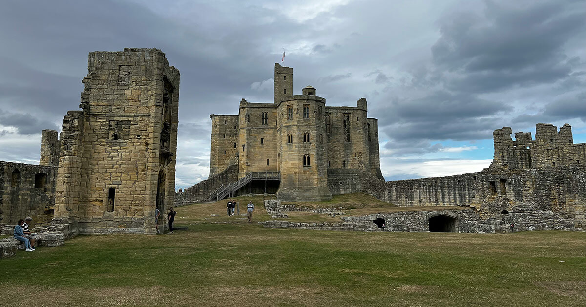 Floodlit medieval castle keep at twilight with dark clouds gathering above the battlements